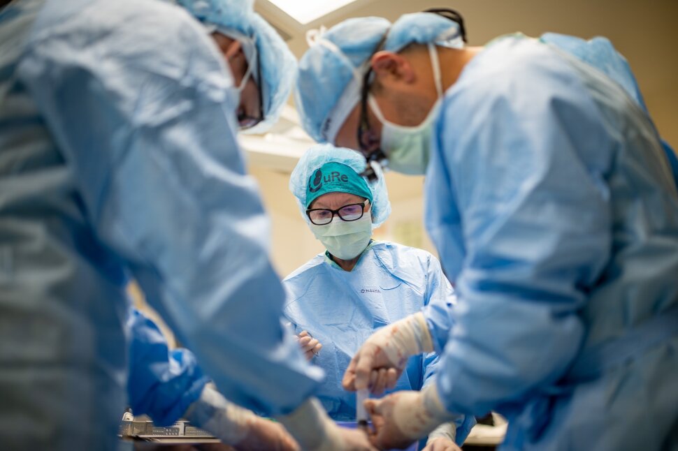People in full scrub caps, masks, and surgical gown look down intently.